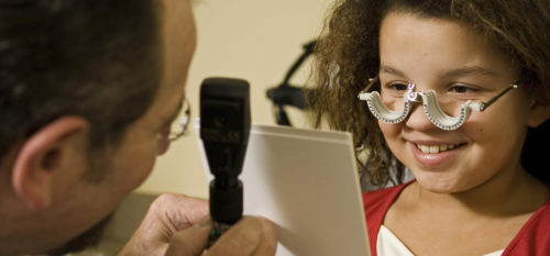 Young child has vision test with doctor checking her eyes while she wears special eye tool.