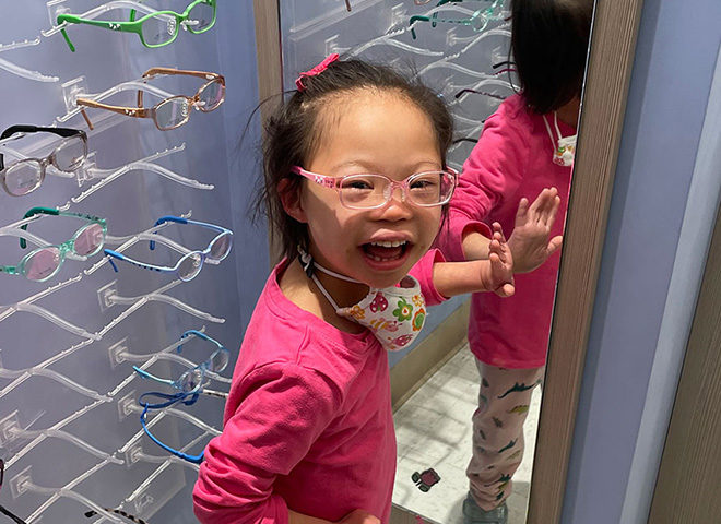 Young child laughing at camera after seeing herself with glasses on.