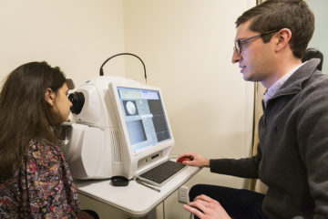 Optometry student using testing a patient's eyes with an optical coherence tomography machine that captures images of the retina.